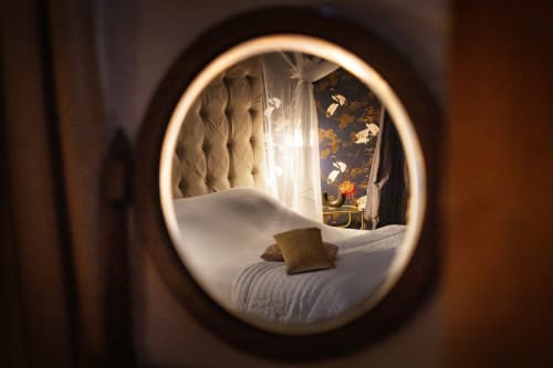 Chambre douillette à l'Alombre B&B à Lectoure avec literie blanche, coussin doré et vue montagne par fenêtre circulaire