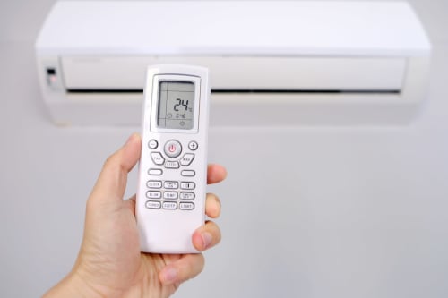Hand holding white AC remote displaying 24 degrees, white split unit air conditioner in background at El Chalecito de