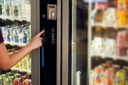 Guest using vending machine keypad at El Chalecito de Alicante hotel, selecting beverage from refrigerated display