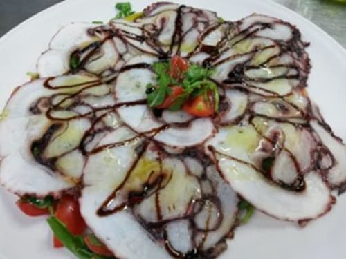 Sliced squid drizzled with dark sauce, garnished with fresh tomatoes and herbs at Hotel Ristorante Domu Incantada in Muravera