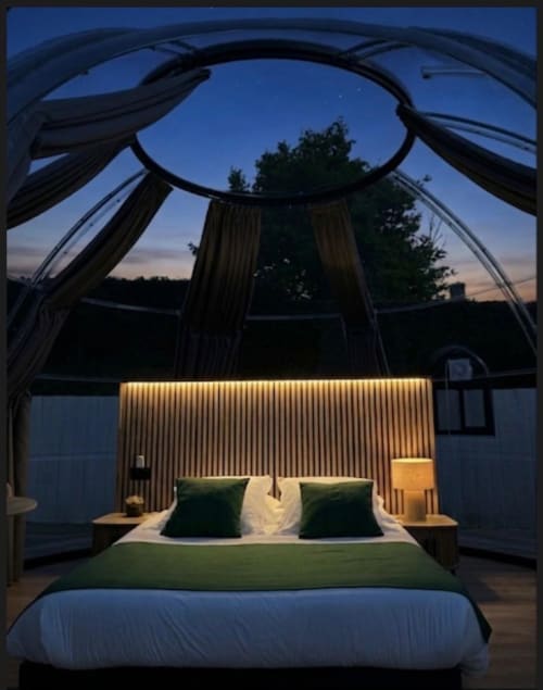 Chambre Bulle Émeraude à Bubble Jade avec plafond dôme transparent, lit king-size aux oreillers verts, luminosité chaleureuse, vue sur le jardin