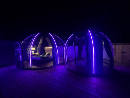 Chambre dôme géodésique illuminée de l'hôtel Bubble Jade aux lumières violettes néon, avec lit et jacuzzi dans le jardin