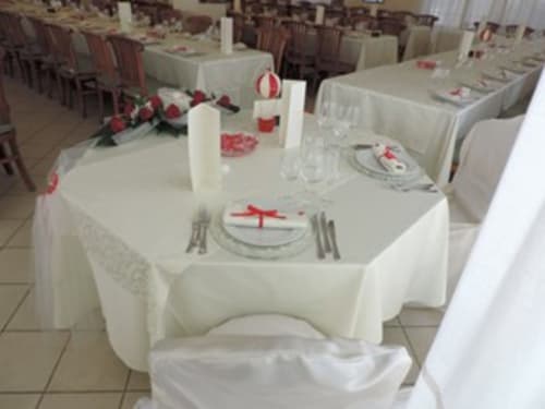 Elegante sala banchetti dell'Hotel Domu Incantada a Muravera con tavoli rotondi, tovaglie bianche, centrotavola floreali rossi e allestimento formale