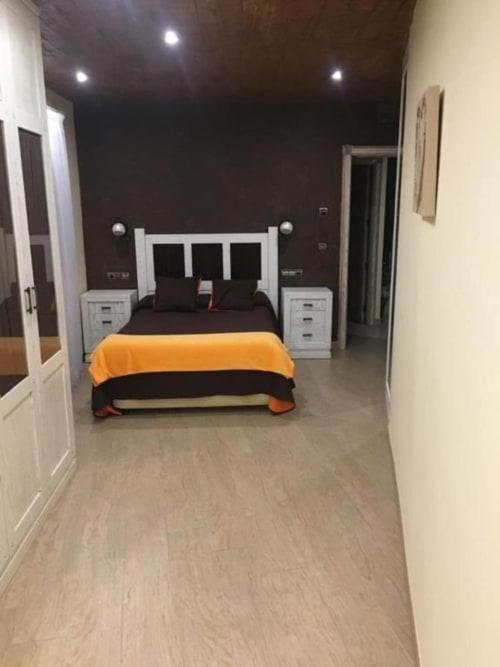 Modern bedroom at Hotel Mulhacén Trevélez with white bed frame, orange throw, dark walls, and twin nightstands in Granada.