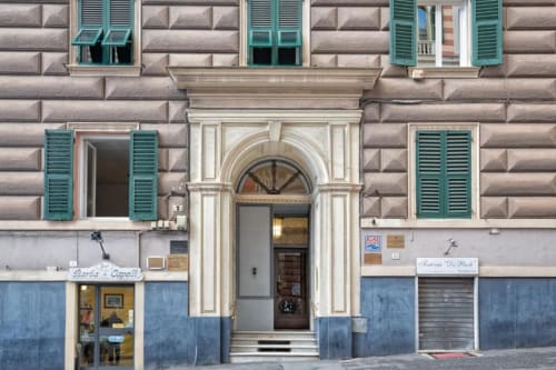 Facciata storica di Le Due Piazze a Genova con persiane turchesi e negozi al piano terra