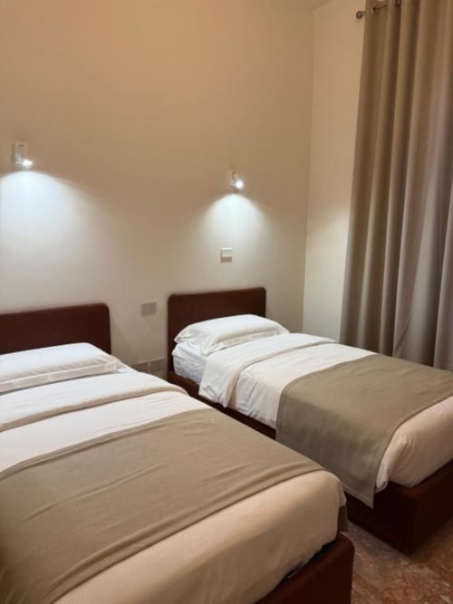 Due letti singoli con biancheria bianca in una moderna camera da letto di Le Due Piazze, Genova, con pareti neutre e beige