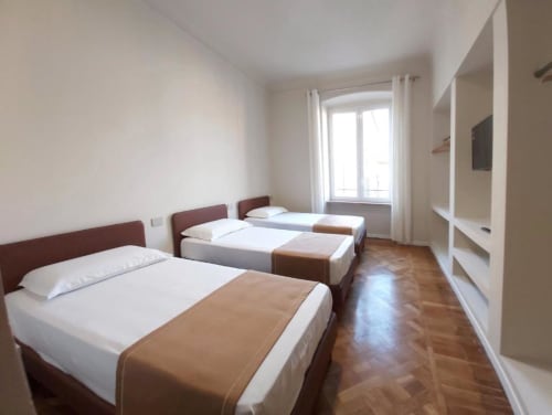 Ampia camera da letto nell'appartamento Le Due Piazze a Genova con tre letti, parquet e balcone con vista città