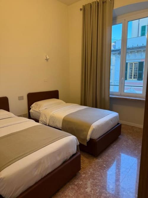 Camera gemella nell'appartamento Le Due Piazze a Genova con vista città, letti in legno scuro, pareti gialle e ampie finestre