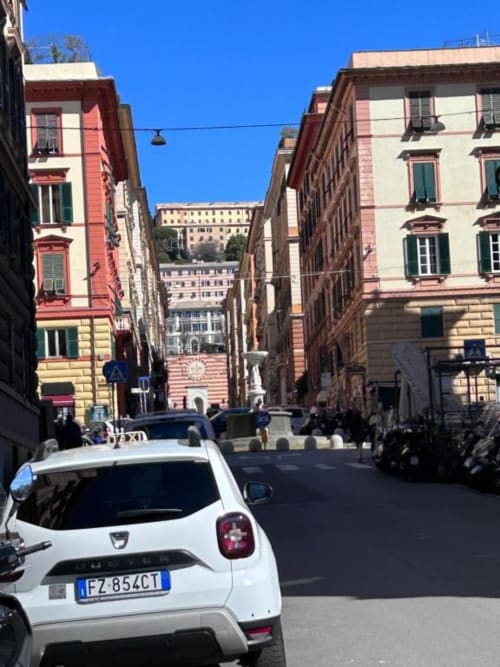 Via di Genova con edifici storici colorati e auto bianca parcheggiata su vicolo ciottolato presso Le Due Piazze
