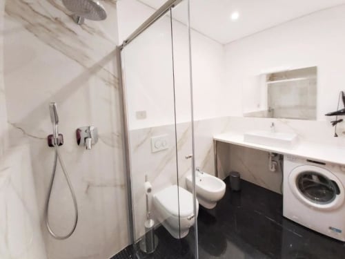 Bagno moderno con doccia a pioggia, wc, mobile con lavatrice integrata e rivestimenti in marmo presso l'appartamento Le Due Piazze