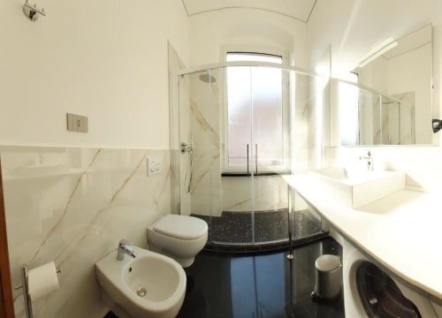Bagno moderno nell'appartamento Le Due Piazze a Genova con piastrelle in marmo, cabina doccia in vetro e doppio lavabo