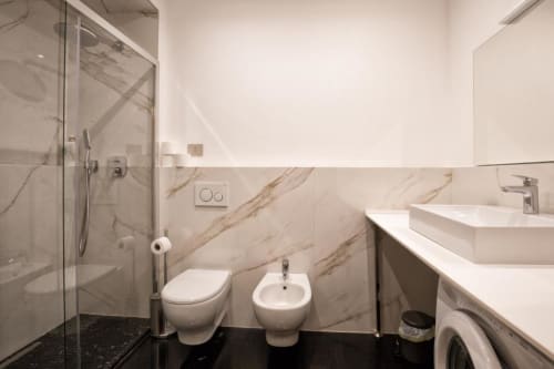 Bagno moderno con piastrelle di marmo, toilette bianca, bidet e doccia a filo pavimento nell'appartamento Le Due Piazze a Genova