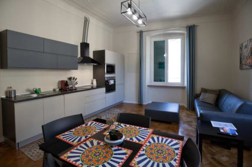 Zona cucina-soggiorno moderna in appartamento 2 camere a Le Due Piazze, Genova, con mobili bianchi, tavolo da pranzo e divano blu