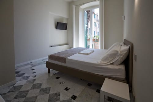 Camera moderna a Le Due Piazze BnB a Genova con letto matrimoniale, biancheria bianca, TV a parete e balcone con vista sulla città