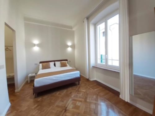 Camera luminosa con letto matrimoniale, pavimento in legno e porte sulla terrazza dell'appartamento Le Due Piazze a Genova