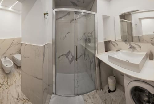 Bagno moderno nell'appartamento Le Due Piazze a Genova con piastrelle in marmo, doccia in vetro curvo, bidet, lavabo e lavatrice.