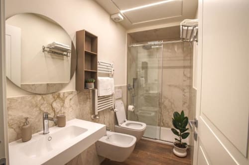 Bagno moderno nell'appartamento Le Due Piazze di Genova con piastrelle in marmo, specchio rotondo, bidet, doccia walk-in e piante