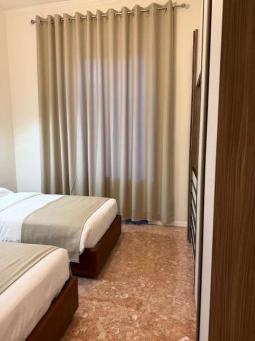 Camera da letto spaziosa nell'appartamento Le Due Piazze a Genova con letti gemelli, tende beige e pavimento in sughero