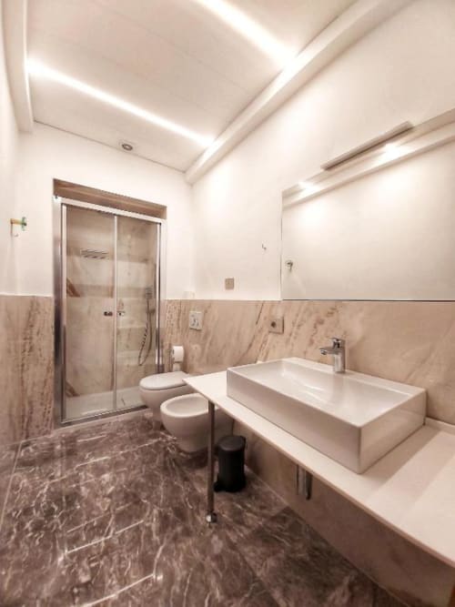 Bagno moderno nell'appartamento Le Due Piazze di Genova con rivestimenti in marmo, lavabo a calice, WC e box doccia in vetro