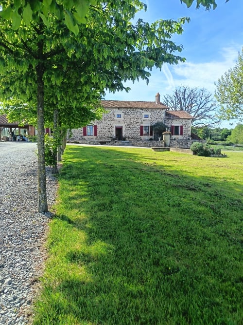Chaumière en pierre du Domaine de Beau Site à Peyrat-de-Bellac, avec pelouse verdoyante et allée bordée d'arbres