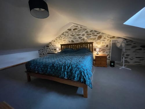 Chambre mansardée cosy au Domaine de Beau Site avec literie bleue à motifs, murs en pierre, lit en bois et lucarnes