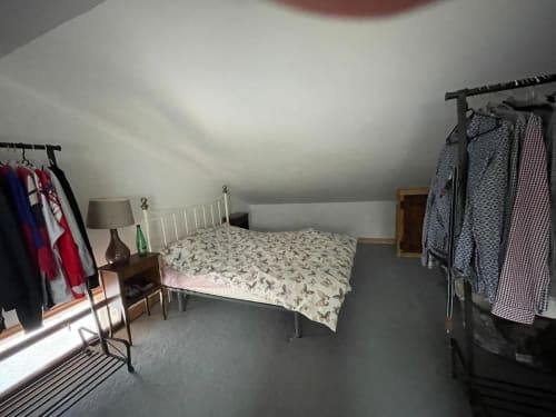 Chambre sous les toits chaleureuse au gîte Domaine de Beau Site avec lit blanc, portants à vêtements et plafond mansardé