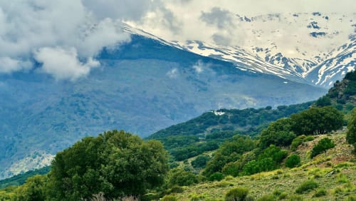 Snow-capped mountain peaks and lush green valleys surrounding Trevélez in Granada, Spain