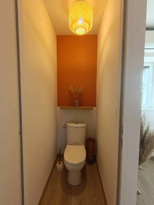 Modern toilet room at Domaine de Beau Site with warm lighting, orange accent wall, and wooden flooring