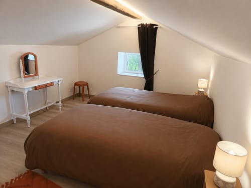 Spacious attic bedroom at Domaine de Beau Site with two brown beds, white desk, and garden view window