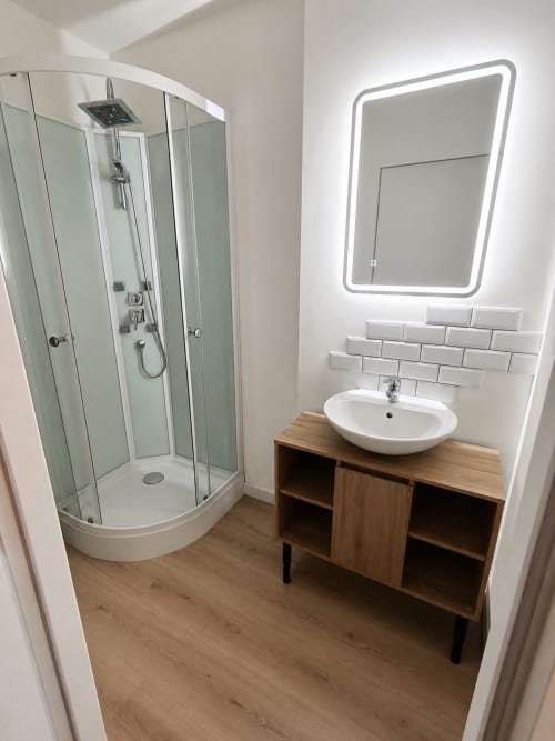 Modern bathroom in Domaine de Beau Site B&B with curved glass shower enclosure, white subway tile, wooden vanity, and