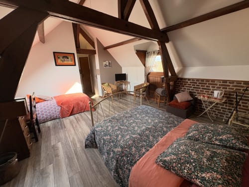 Cozy attic bedroom at Ferme de la Forterie with exposed beams, floral patterned beds, brick fireplace, and garden views in