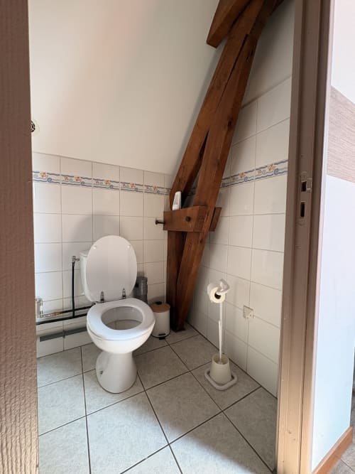 Rustic bathroom with white toilet and decorative wooden beam at Ferme de la Forterie Verlinghem, Verlinghem