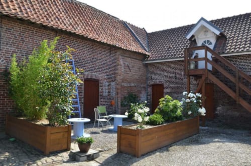 Courtyard garden at Ferme de la Forterie with brick buildings, wooden planters, white flowers, and outdoor seating area in