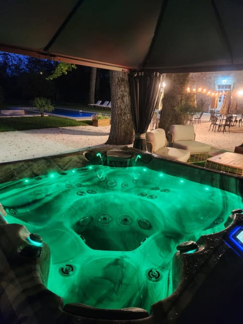 Illuminated hot tub at Château de la Rochetière, Marcilloles, with pool and terrace visible at night