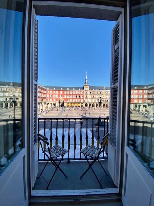 Balcony view of Plaza Mayor Madrid from apartment with two chairs, historic red buildings, and clear blue sky
