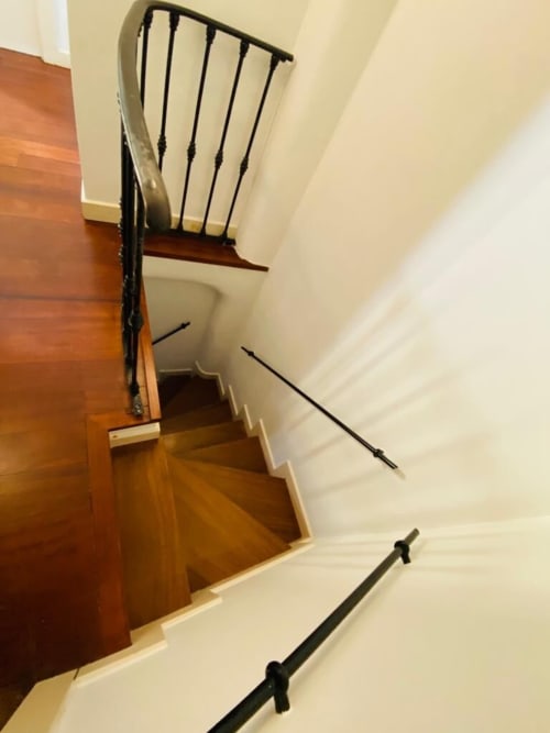 Wooden staircase with black metal railings in Plaza Mayor apartment, cream walls and polished wood steps