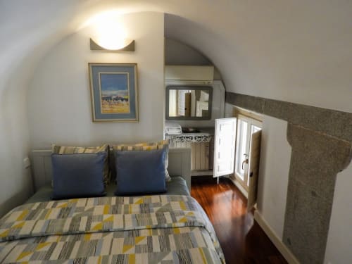 Cozy attic bedroom with striped bedding, blue pillows, TV, and arched ceiling in Plaza Mayor apartment
