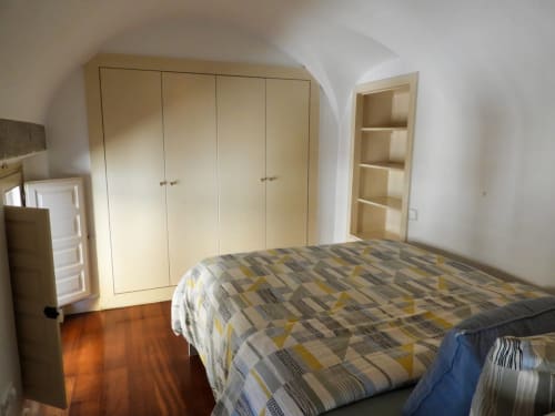 Spacious bedroom with patterned bedding, cream wardrobe, built-in shelving, and wooden flooring in Plaza Mayor apartment