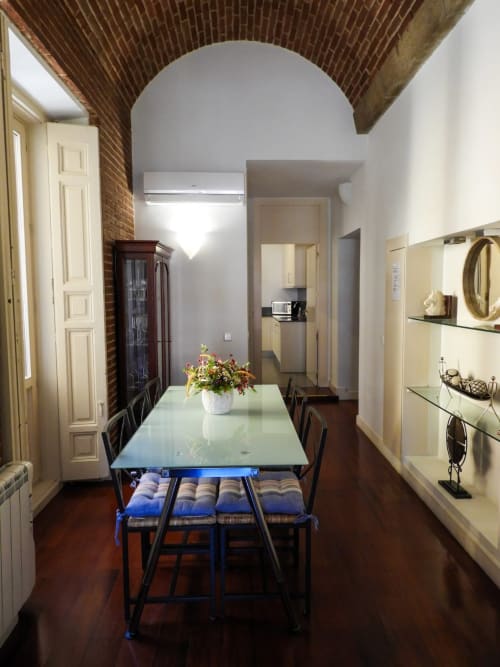 Modern apartment dining room with glass table, exposed brick ceiling, and kitchen access at Charming view Plaza Mayor, Madrid