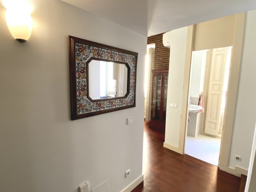 Modern hallway in Plaza Mayor apartment with decorative mirror, hardwood floors, cream doors, and brick accent wall