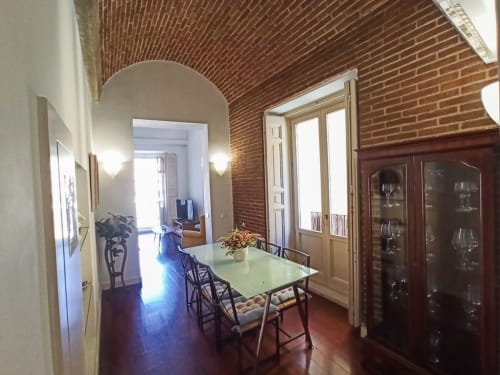 Dining area in Plaza Mayor apartment with brick vaulted ceiling, green table, wooden chairs, and glass cabinet display