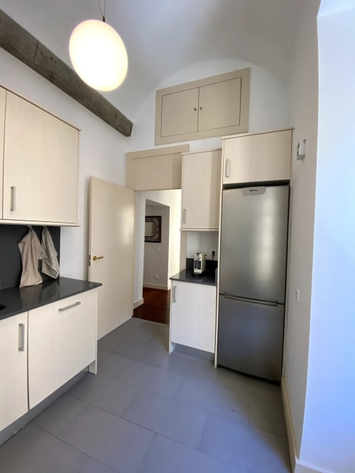Modern kitchen in Plaza Mayor apartment with white cabinetry, stainless steel appliances, black countertops, and pendant