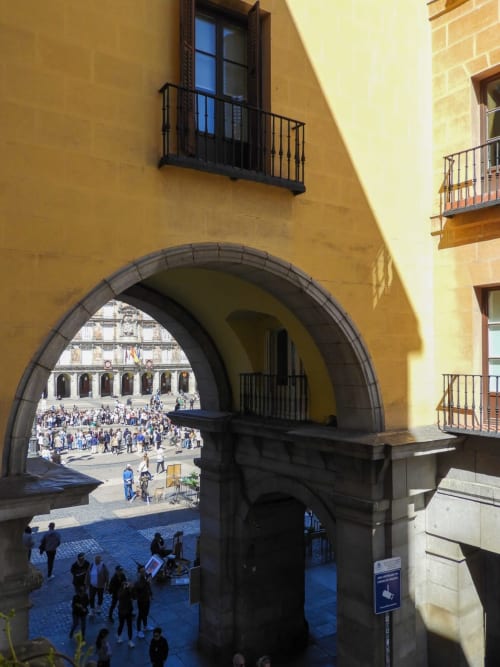 Archway view of Plaza Mayor Madrid from apartment balcony with crowds and historic buildings