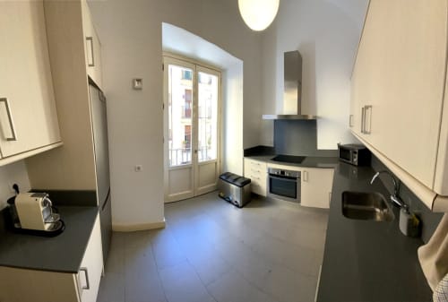 Modern kitchen with black countertops, cream cabinets, stainless steel appliances, and balcony doors in Madrid apartment