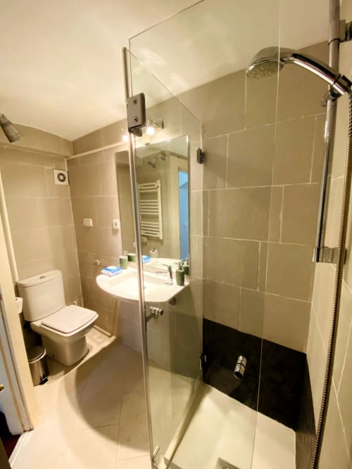 Modern bathroom in Plaza Mayor apartment with glass shower, white sink, toilet, and cream tile walls.