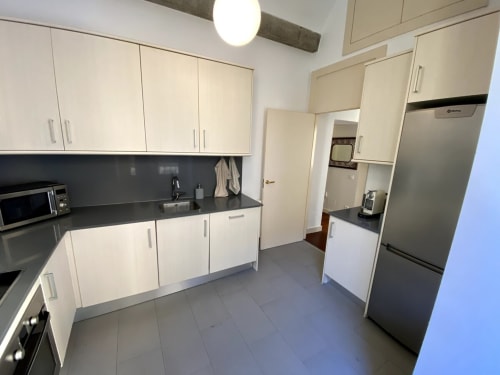 Modern kitchen in Plaza Mayor apartment with cream cabinets, black countertop, stainless steel appliances, and tile flooring