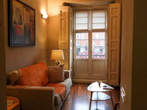 Elegant studio apartment at Plaza Mayor hotel with orange accents, wooden doors opening to city balcony view, warm lighting,