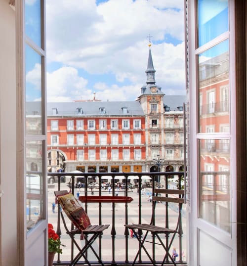 View from balcony of Plaza Mayor with red colonial architecture, bell tower, and outdoor seating in Madrid apartment