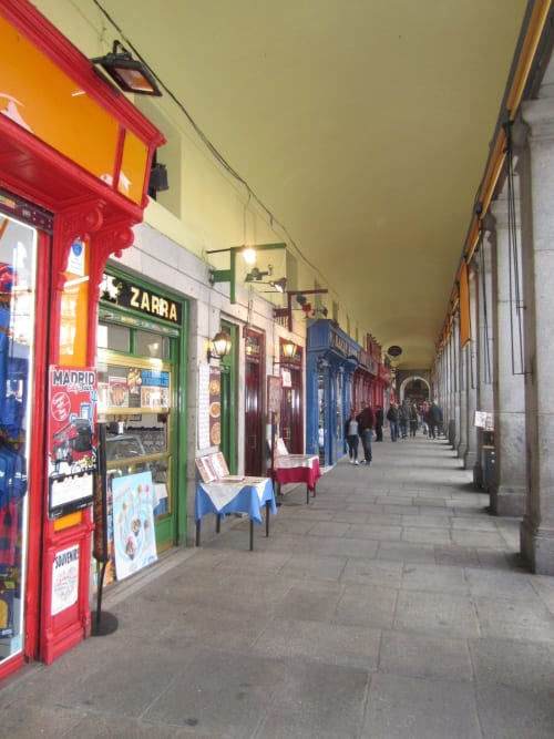 Colorful arcade and shop storefronts along a covered street in Madrid's Plaza Mayor neighborhood