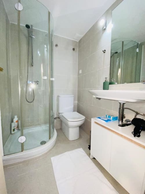 Modern bathroom in Plaza Mayor apartment with glass shower enclosure, white fixtures, vanity sink, and tiled walls